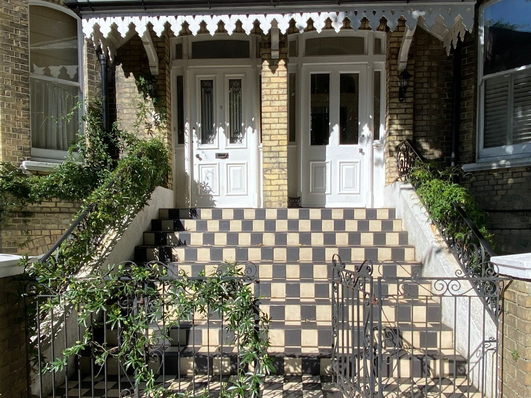 A Victorian house entrance with checkered tiled steps and ornate ironwork.