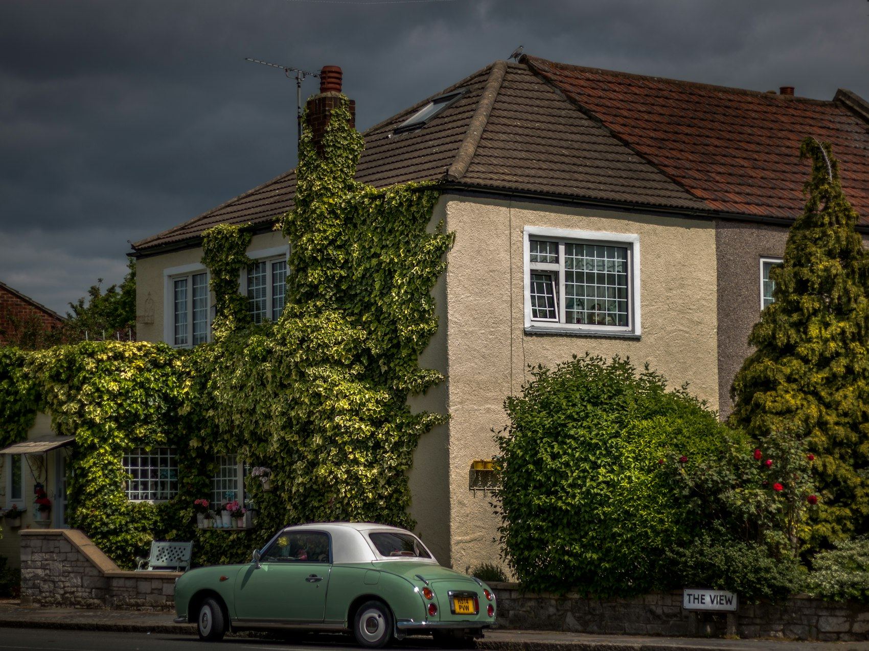 A 1930s style house with a bay window and a car parked outside.