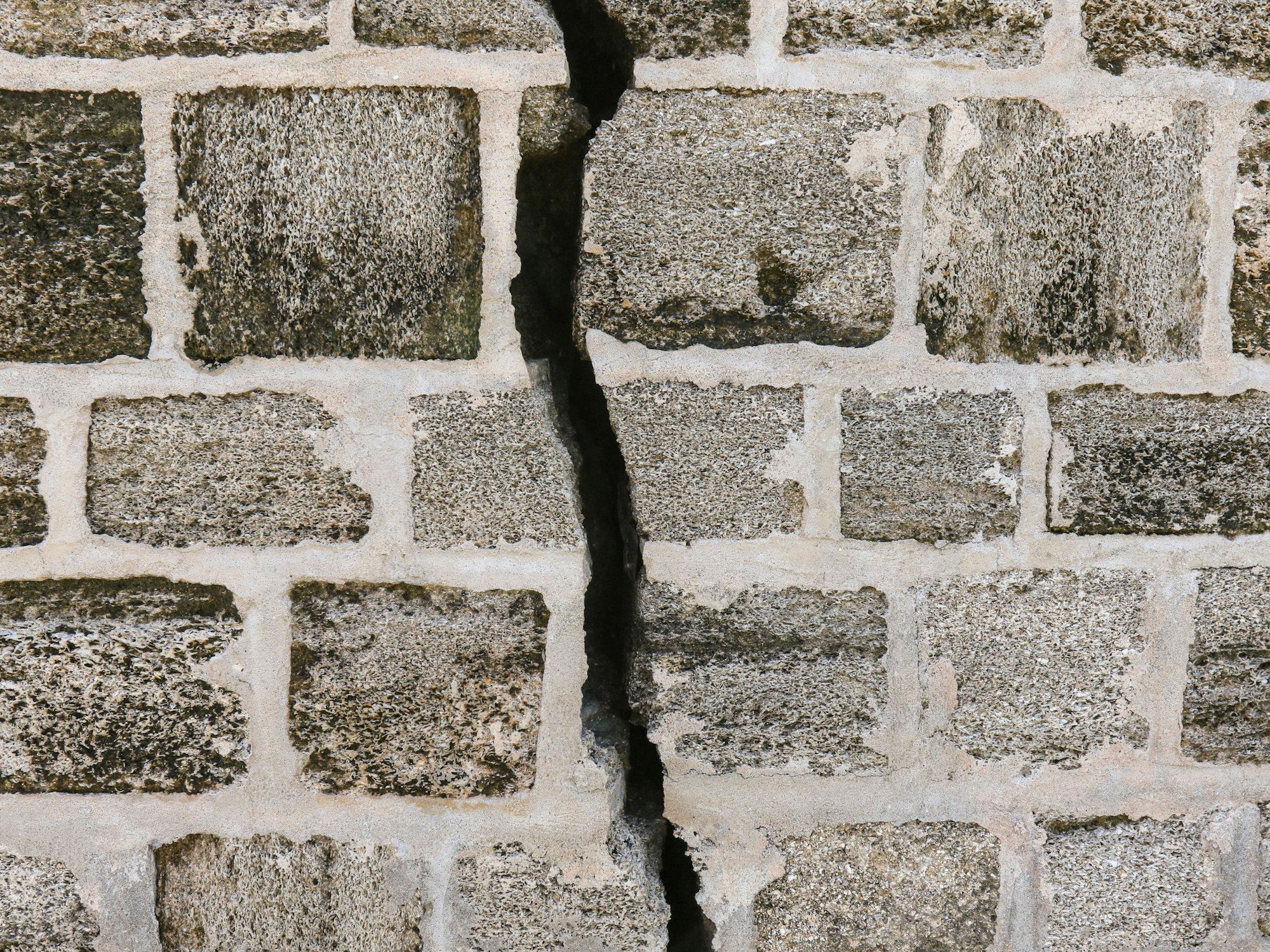 A vertical crack running down a grey brick wall.